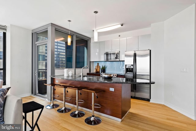 kitchen with sink, decorative light fixtures, light hardwood / wood-style flooring, appliances with stainless steel finishes, and a kitchen bar