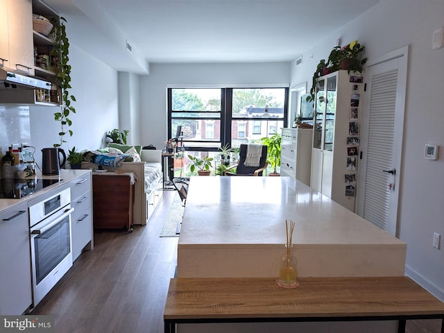 kitchen with white cabinetry, a kitchen island, dark hardwood / wood-style flooring, stainless steel oven, and black electric stovetop