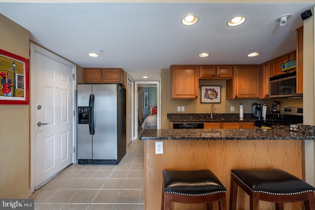 kitchen with a kitchen breakfast bar, dark stone counters, kitchen peninsula, and stainless steel appliances