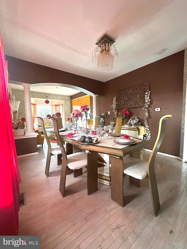 dining area featuring hardwood / wood-style flooring, ornate columns, and a notable chandelier