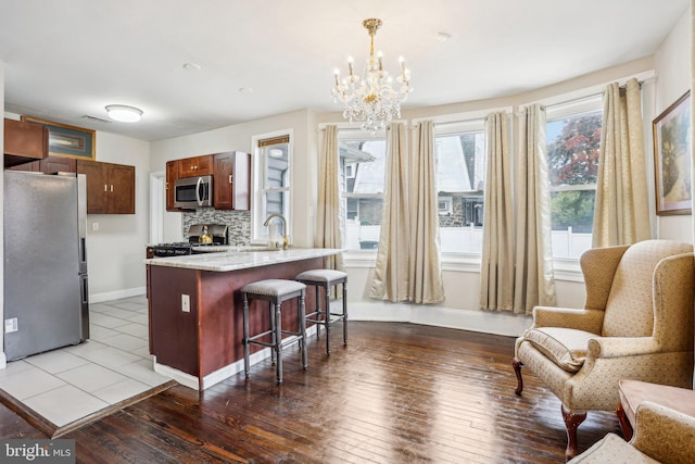 kitchen with hanging light fixtures, wood-type flooring, backsplash, appliances with stainless steel finishes, and a breakfast bar