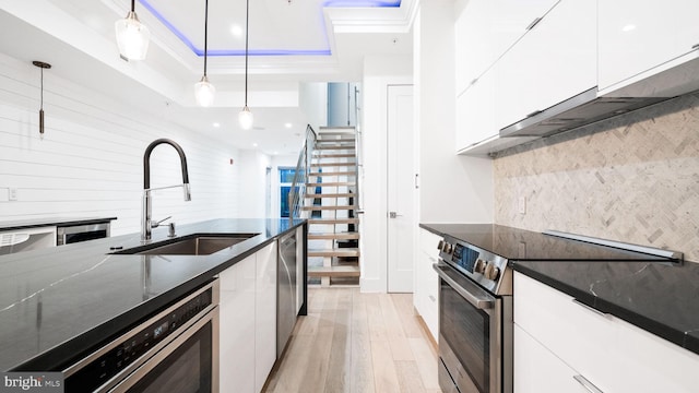 kitchen with appliances with stainless steel finishes, light wood-type flooring, white cabinetry, dark stone counters, and pendant lighting