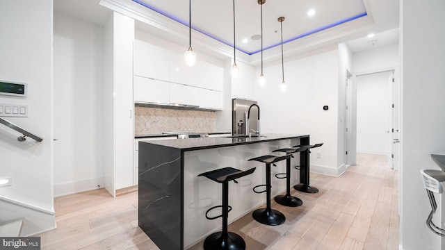 kitchen featuring a raised ceiling, white cabinetry, light wood-type flooring, sink, and decorative light fixtures