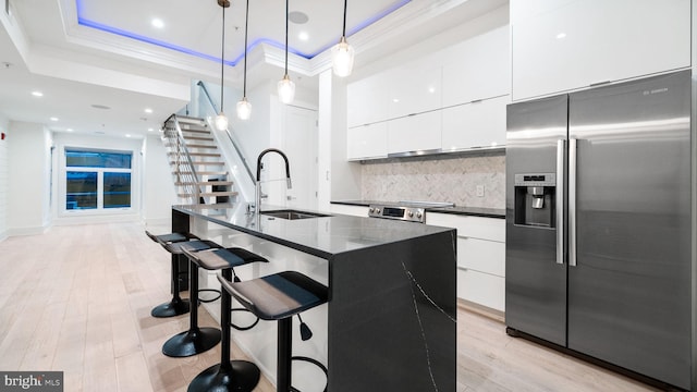 kitchen featuring appliances with stainless steel finishes, light wood-type flooring, a tray ceiling, decorative light fixtures, and a center island with sink