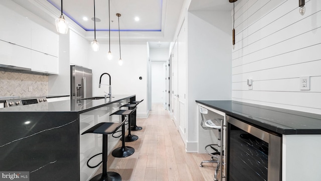 kitchen with light hardwood / wood-style flooring, stainless steel appliances, wine cooler, pendant lighting, and white cabinets