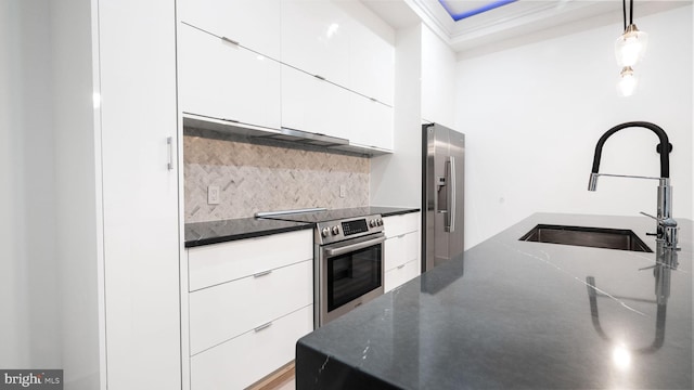 kitchen with hanging light fixtures, stainless steel appliances, dark stone counters, sink, and white cabinetry