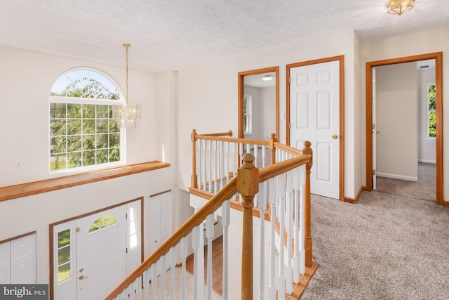 hall featuring light colored carpet, a textured ceiling, and a notable chandelier