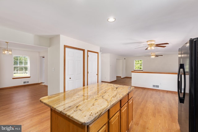 kitchen featuring light hardwood / wood-style floors, a center island, ceiling fan with notable chandelier, light stone countertops, and refrigerator