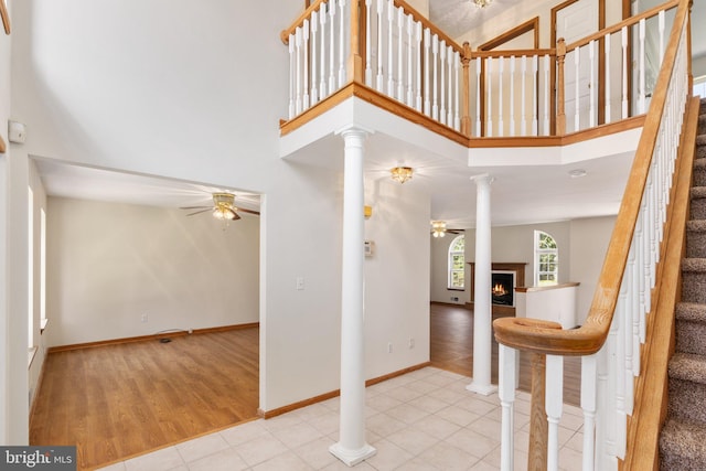 entryway with a towering ceiling, light hardwood / wood-style floors, ceiling fan, and ornate columns