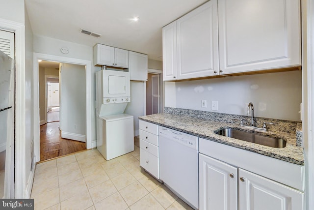 kitchen with white cabinets, white dishwasher, sink, light hardwood / wood-style flooring, and stacked washing maching and dryer