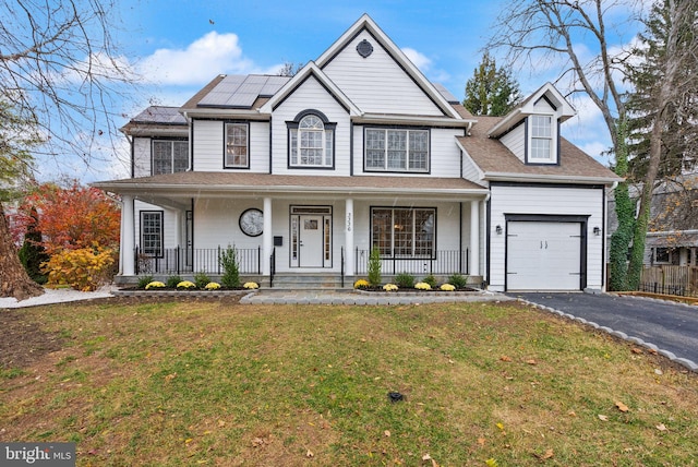 view of front of home featuring covered porch, solar panels, a garage, and a front yard