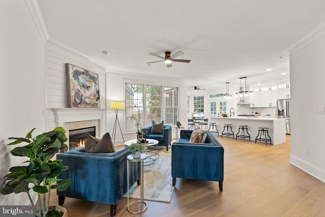 living room with ceiling fan, sink, light wood-type flooring, and crown molding