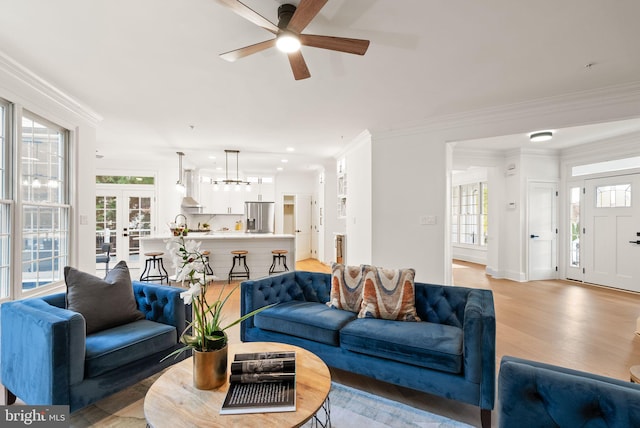 living room featuring crown molding, french doors, ceiling fan, and light wood-type flooring