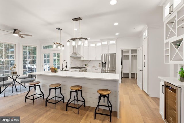 kitchen featuring ceiling fan, wall chimney exhaust hood, beverage cooler, stainless steel appliances, and decorative light fixtures