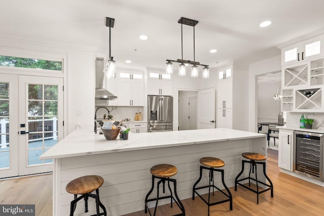 kitchen with white cabinets, wall chimney range hood, tasteful backsplash, stainless steel fridge with ice dispenser, and beverage cooler