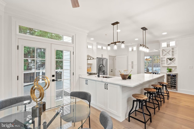 kitchen featuring pendant lighting, white cabinets, ornamental molding, light hardwood / wood-style floors, and beverage cooler