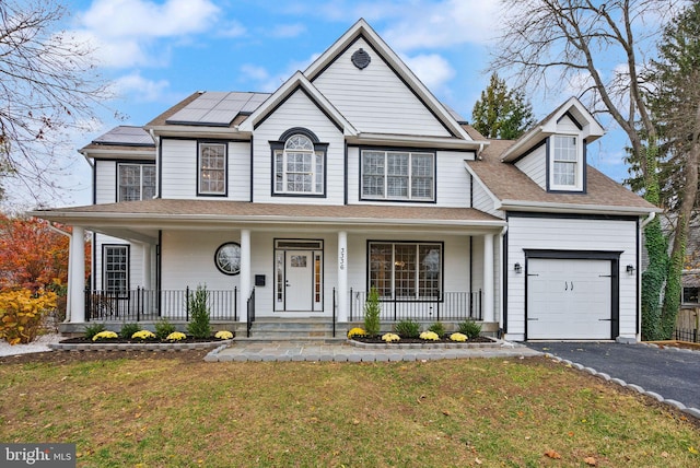 view of front of house with a front lawn, a garage, a porch, and solar panels