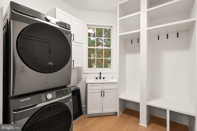 clothes washing area with sink, cabinets, light wood-type flooring, and stacked washer / dryer