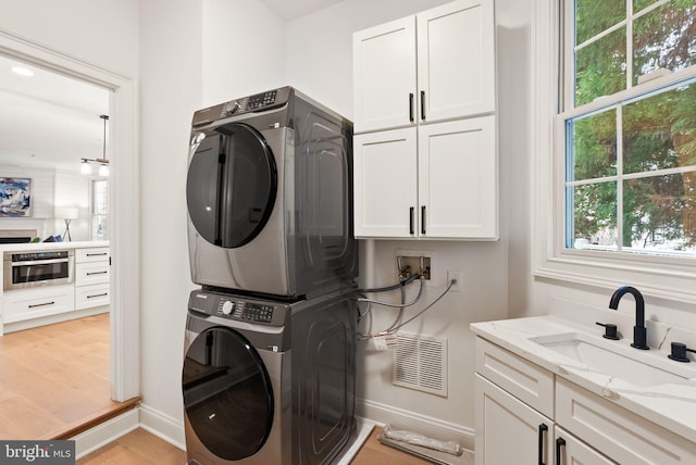 washroom with cabinets, light hardwood / wood-style floors, stacked washer / drying machine, and sink