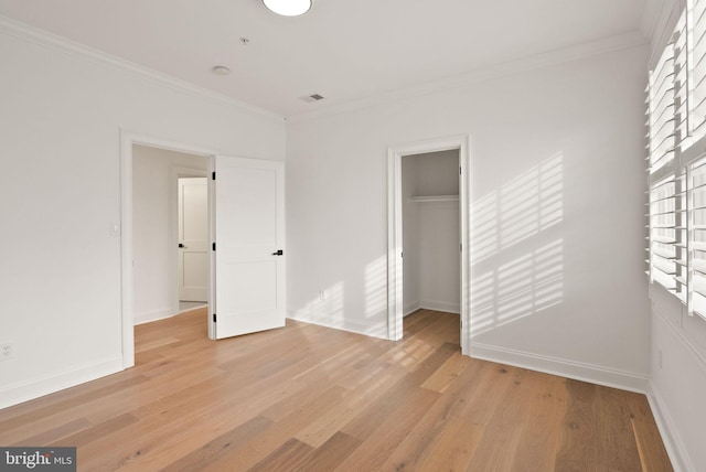 unfurnished bedroom featuring a walk in closet, light hardwood / wood-style flooring, a closet, and ornamental molding