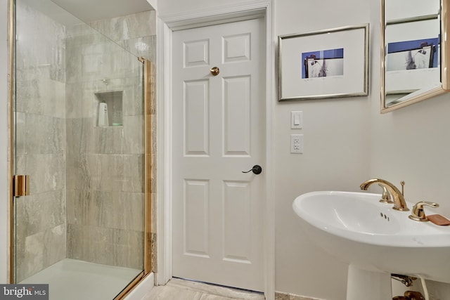 bathroom featuring a shower with shower door and sink