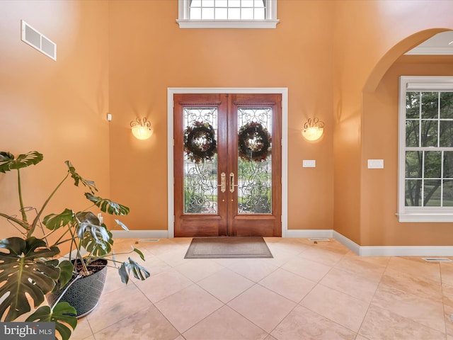 entryway with a wealth of natural light, french doors, a towering ceiling, and crown molding