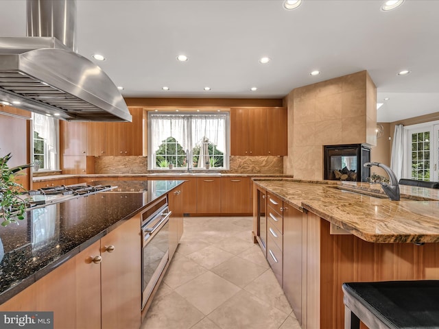 kitchen with tasteful backsplash, island exhaust hood, dark stone countertops, and appliances with stainless steel finishes