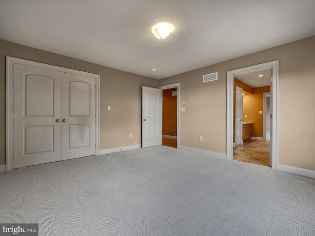 unfurnished bedroom with ensuite bath, light carpet, and a closet