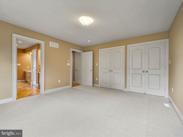 unfurnished bedroom featuring multiple closets and light colored carpet