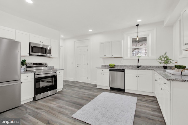 kitchen with stainless steel appliances, white cabinets, hardwood / wood-style flooring, and hanging light fixtures