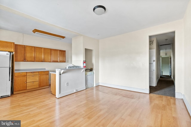 kitchen with white refrigerator, light hardwood / wood-style flooring, kitchen peninsula, and washer / dryer