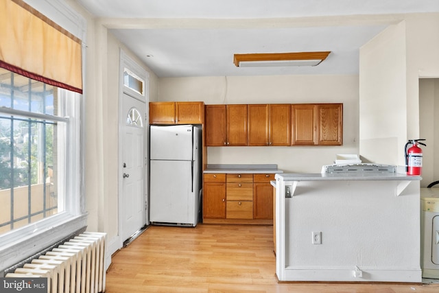 kitchen featuring kitchen peninsula, white refrigerator, radiator heating unit, and light hardwood / wood-style floors