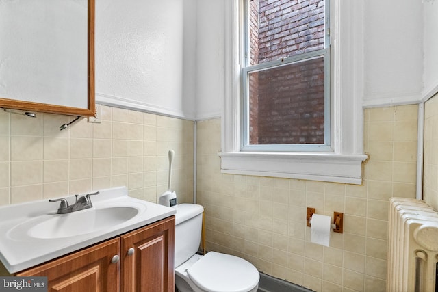 bathroom featuring vanity, radiator heating unit, tile walls, toilet, and a wealth of natural light