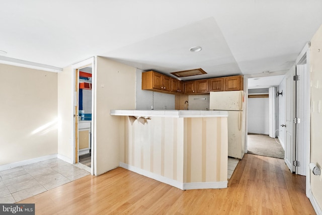 kitchen with a kitchen bar, light hardwood / wood-style floors, white fridge, and kitchen peninsula