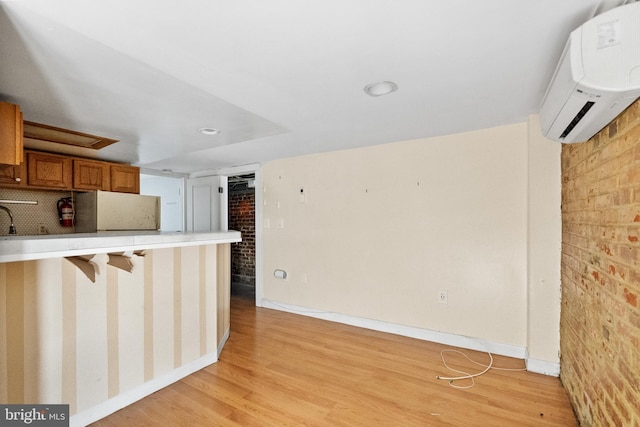 kitchen with brick wall, light hardwood / wood-style floors, and a wall unit AC