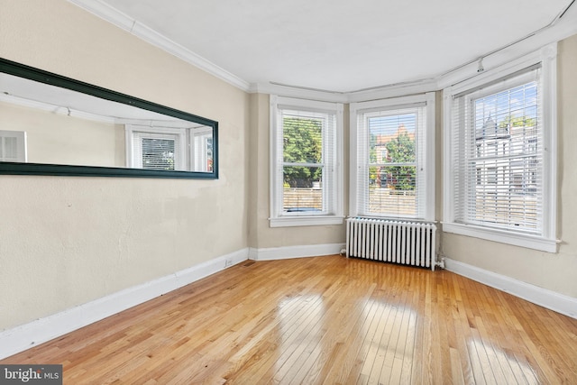 empty room with radiator, hardwood / wood-style flooring, ornamental molding, and a wealth of natural light