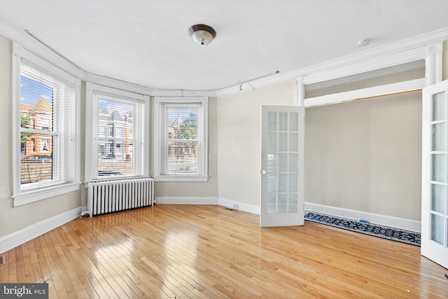 empty room featuring french doors, hardwood / wood-style flooring, ornamental molding, and radiator heating unit