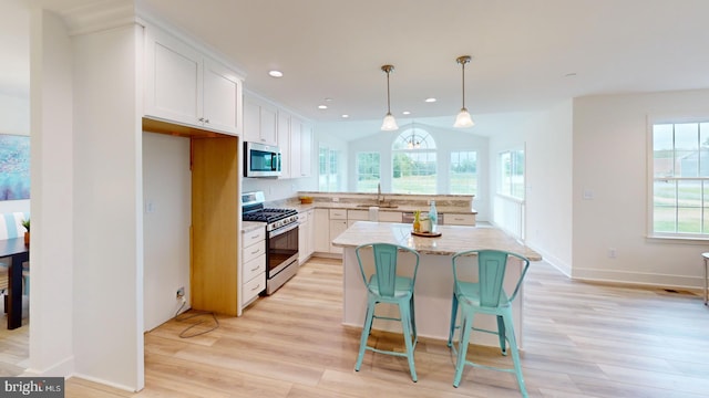 kitchen featuring stainless steel appliances, white cabinets, a wealth of natural light, and a center island