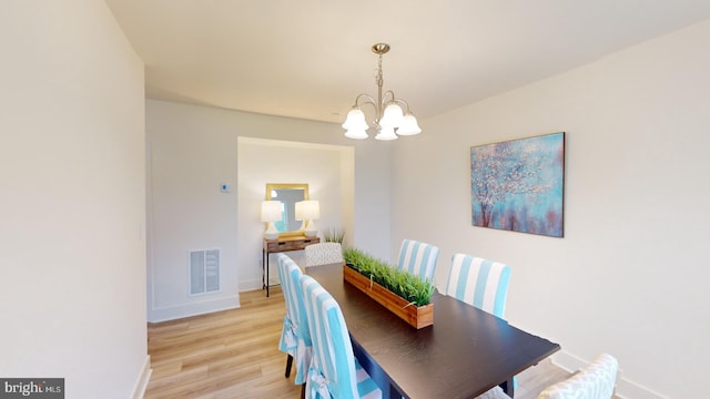 dining area with light wood-type flooring and an inviting chandelier