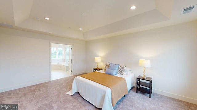 bedroom featuring a raised ceiling, ensuite bathroom, and carpet