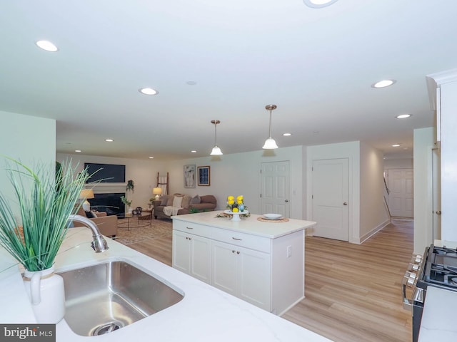 kitchen featuring white cabinets, hanging light fixtures, sink, range, and light hardwood / wood-style floors