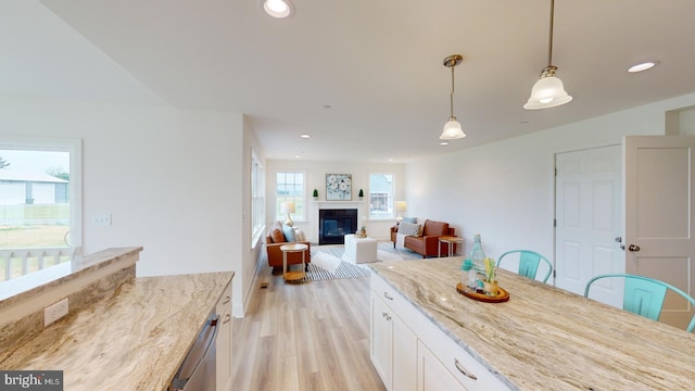 kitchen with light wood-type flooring, white cabinetry, light stone countertops, and pendant lighting