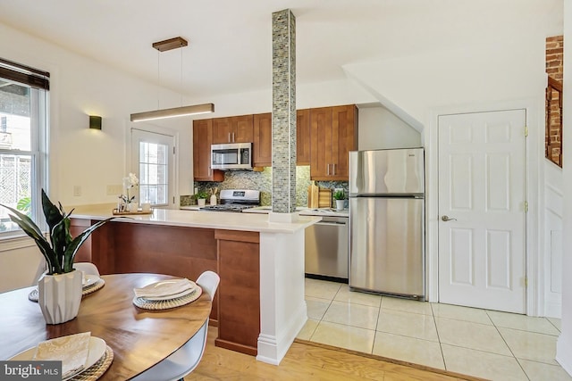 kitchen with appliances with stainless steel finishes, hanging light fixtures, kitchen peninsula, and a healthy amount of sunlight