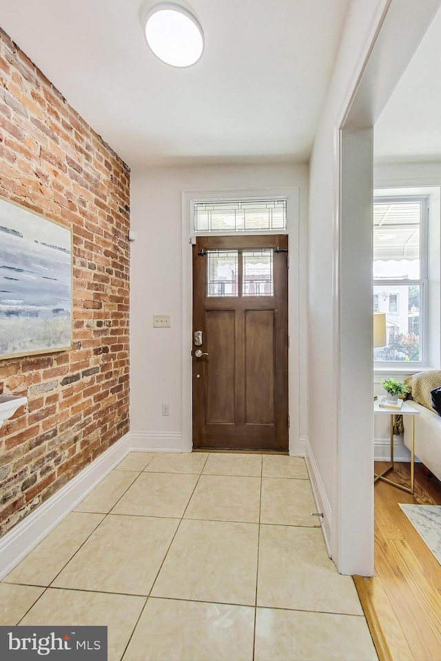 foyer entrance featuring light wood-type flooring, a healthy amount of sunlight, and brick wall