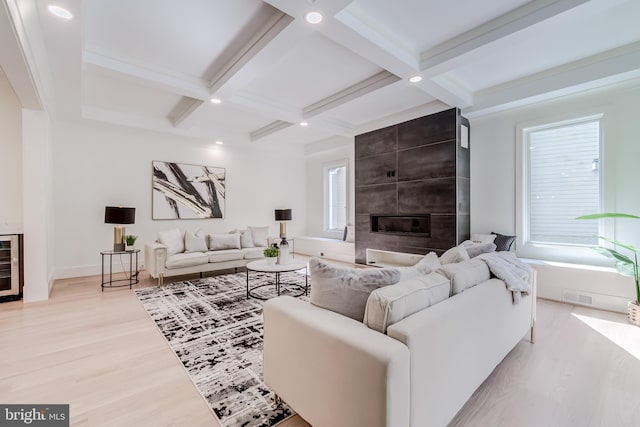 living room with beam ceiling, a tiled fireplace, light wood-type flooring, and coffered ceiling