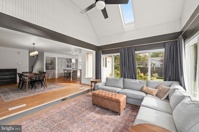 living room featuring hardwood / wood-style flooring, ceiling fan with notable chandelier, a skylight, and high vaulted ceiling