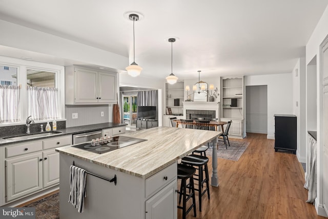 kitchen featuring sink, a kitchen island, black electric cooktop, dark hardwood / wood-style floors, and a fireplace