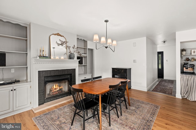 dining space featuring a brick fireplace, a notable chandelier, and light hardwood / wood-style floors