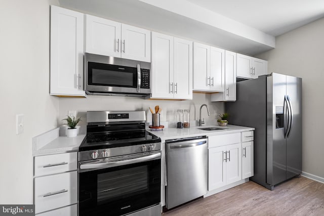 kitchen with white cabinets, stainless steel appliances, sink, and light hardwood / wood-style flooring