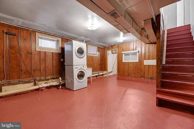 basement featuring wood walls and stacked washing maching and dryer